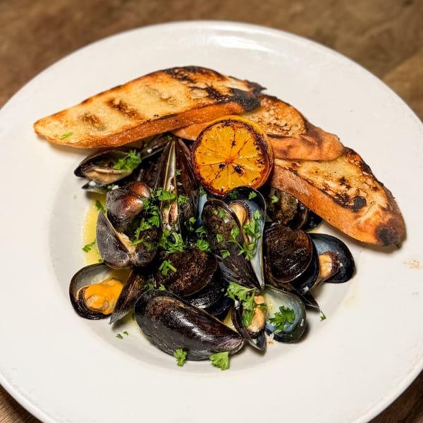 Steamed mussels in a white wine sauce with grilled bread and a charred lemon slice.