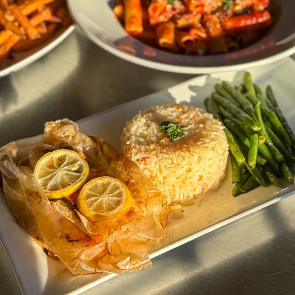 Baked fish with lemon slices, rice pilaf, and green beans on a white plate.