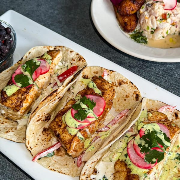 Three grilled fish tacos with radish, cilantro, and green sauce, served with black beans and plantains.