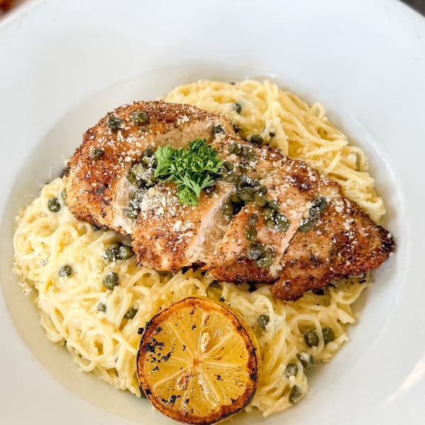 Breaded chicken with capers and parsley over pasta, garnished with a grilled lemon slice.