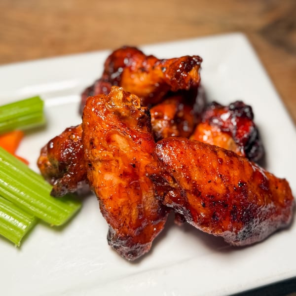 Three Blind Mice's glazed chicken wings with celery sticks and carrot slices on a white plate.