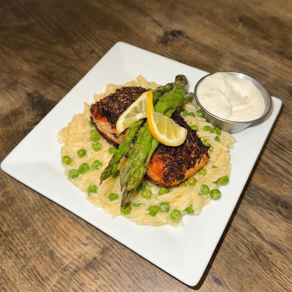 Two pieces of blackened salmon with asparagus and lemon on a bed of orzo pasta and peas.